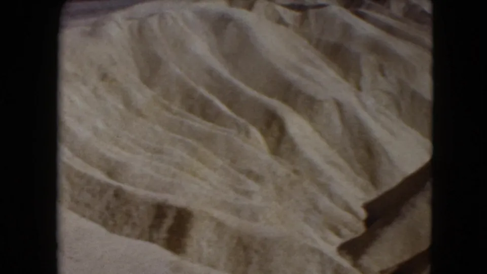 1961 Nevada 8mm frame showing sweeping dune curves, darker grooves, and layered sand texture without visible people or structures.