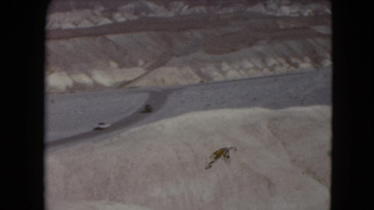 A curving desert road crosses pale hills with tiny cars visible.