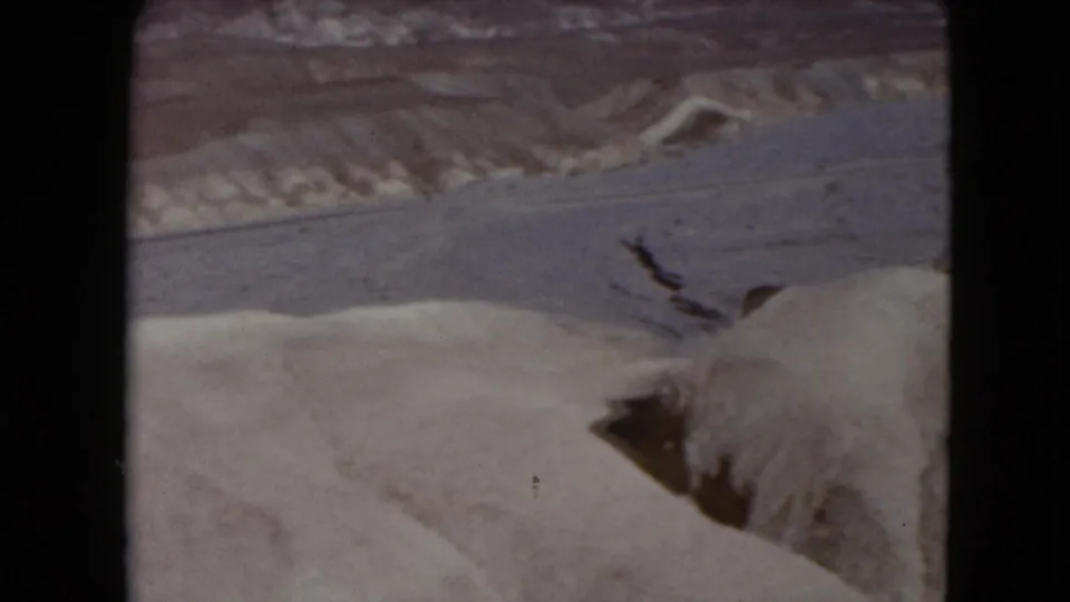 Soft 1961 Nevada 8mm frame of a winding road and small cars set among sandy washes and rock formations.