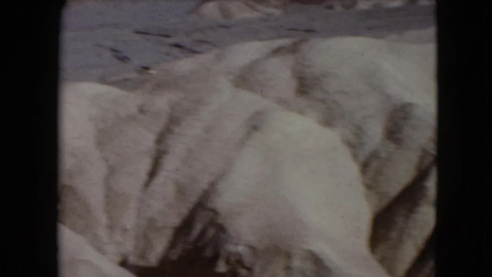 Nevada desert rocks and sandy slopes dominate the frame, with the winding roadway receding in the background.