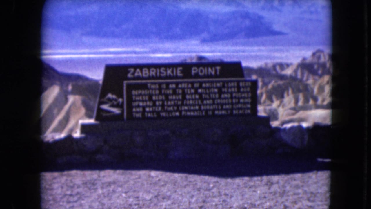1961 8mm frame of the Zabriskie Point informational sign with pale desert ridges and blue-shifted sky behind it.