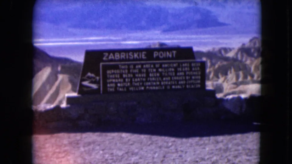 Handheld 8mm frame of the Zabriskie Point sign, showing the title, text block, foreground shadow, and pale desert ridges.