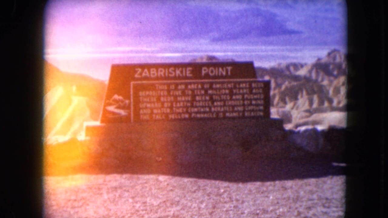 Zabriskie Point sign in front of desert hills with a bright light leak at the left edge.