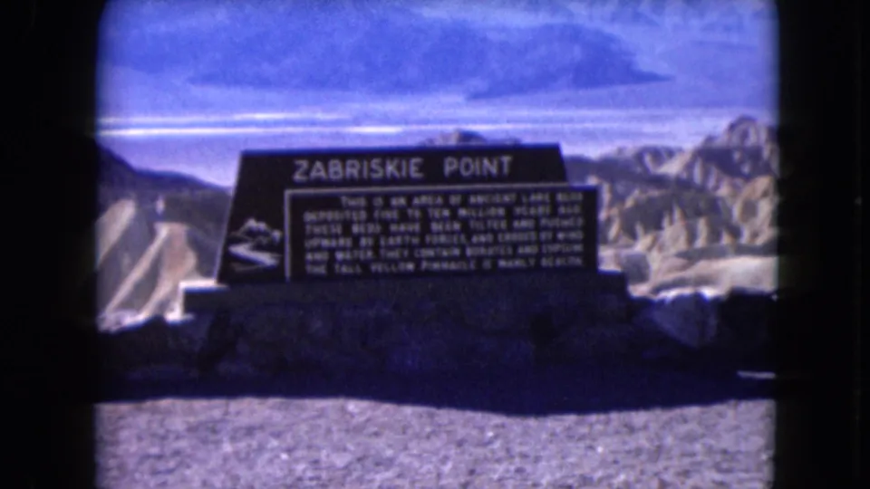 Blue-shifted 1961 8mm frame showing the Zabriskie Point marker, foreground gravel, and eroded desert hills.