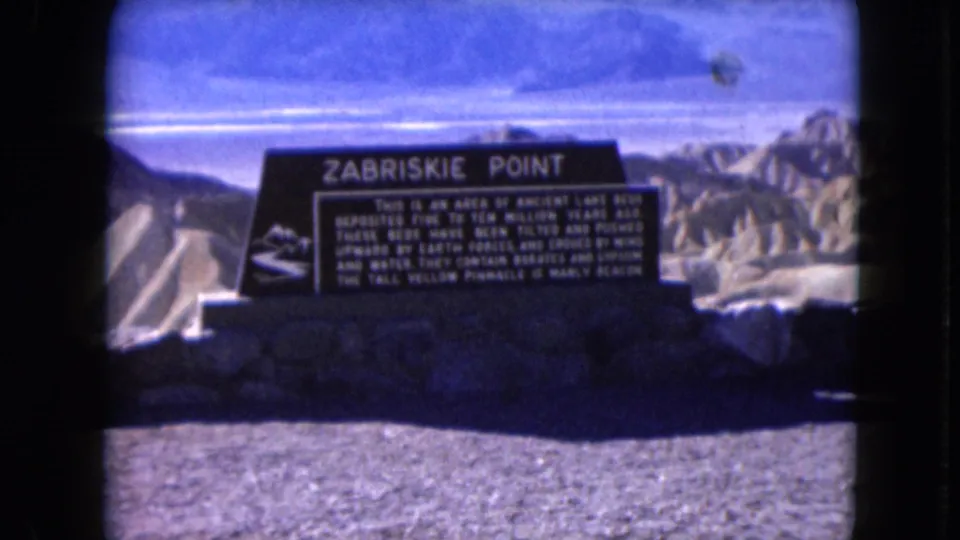 A handheld 1961 8mm frame shows the Zabriskie Point sign with sunlit desert formations beyond.