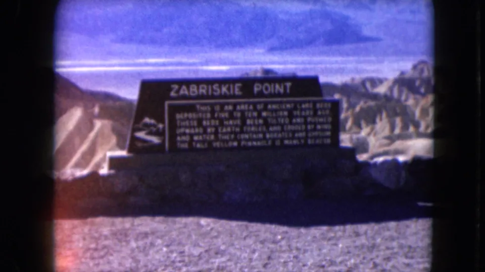 1961 8mm view of the Zabriskie Point sign, with readable heading, gravel foreground, and eroded desert formations behind.