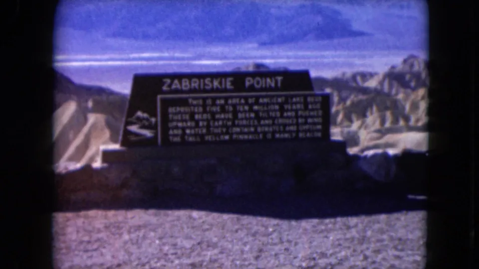 Centered 1961 home-movie frame of the Zabriskie Point sign and surrounding Nevada desert landscape.