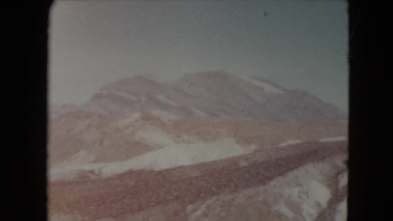 1961 Nevada 8mm frame with a broad mountain ridge, light snow patches, and dry rocky hills in the foreground.