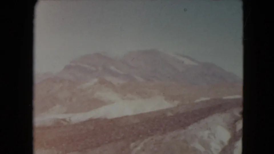 1961 Nevada 8mm frame with a broad mountain ridge, light snow patches, and dry rocky hills in the foreground.