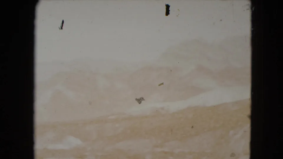1961 Nevada 8mm frame where the mountain landscape appears washed by bright exposure, with dust and small film marks visible.