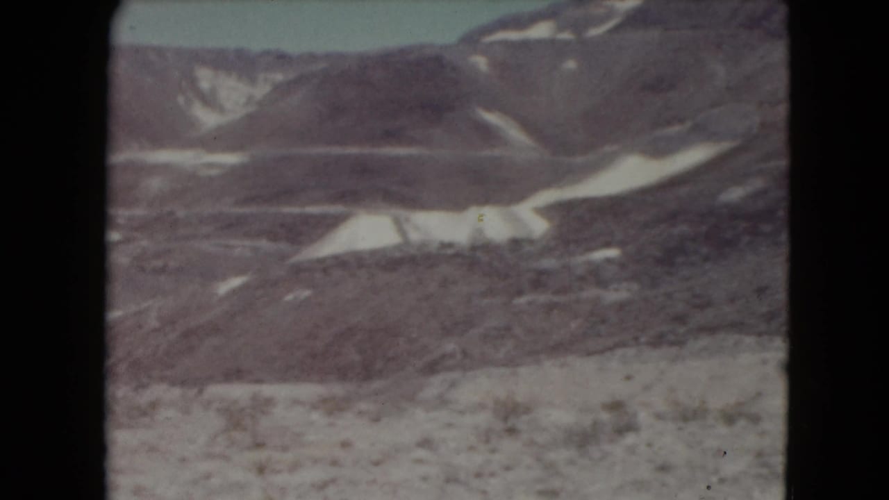 Rugged desert hills with pale snow patches beneath a washed sky.