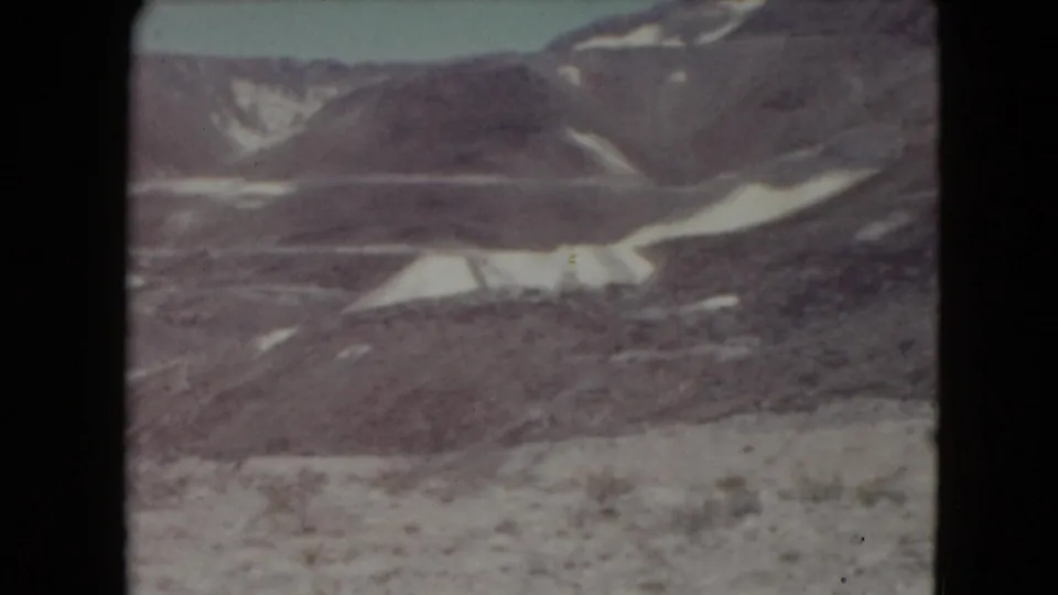 1961 Nevada 8mm frame showing distant rocky hills with snow patches and open desert foreground.