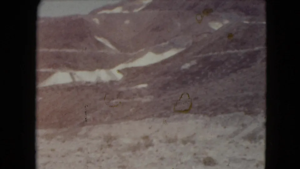 Vintage Nevada home-movie frame of a rugged slope with snow patches, muted color, and dust marks.