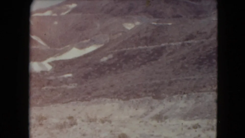 1961 Nevada 8mm view of barren hillsides and light snow across rocky desert terrain.