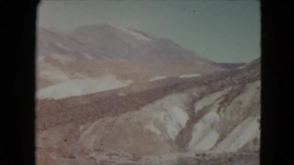 1961 Nevada home-movie frame with layered desert hills, snow-lined gullies, and a pale sky.