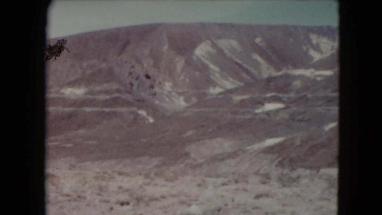 1961 8mm home-movie view of remote Nevada desert hills, pale sky, and eroded mountain slopes with no people or structures visible.