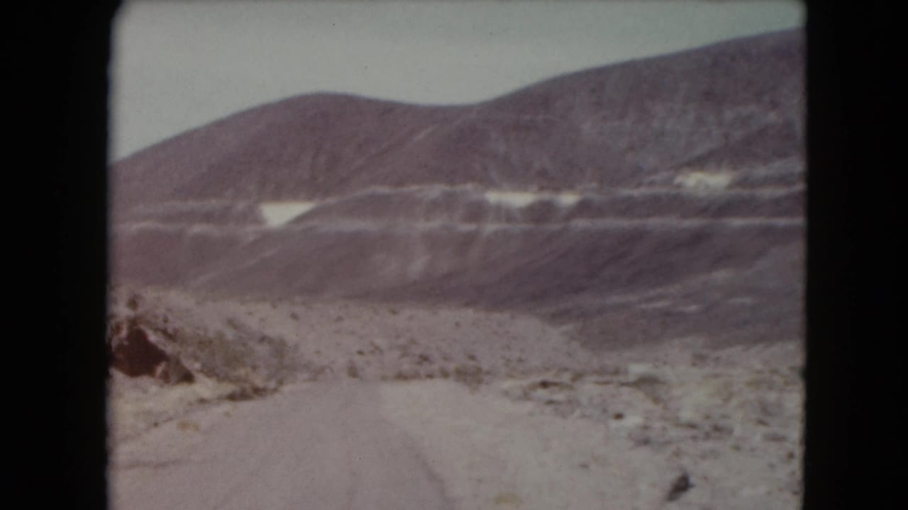 Dirt road entering a rocky desert valley with layered mountains in the background.