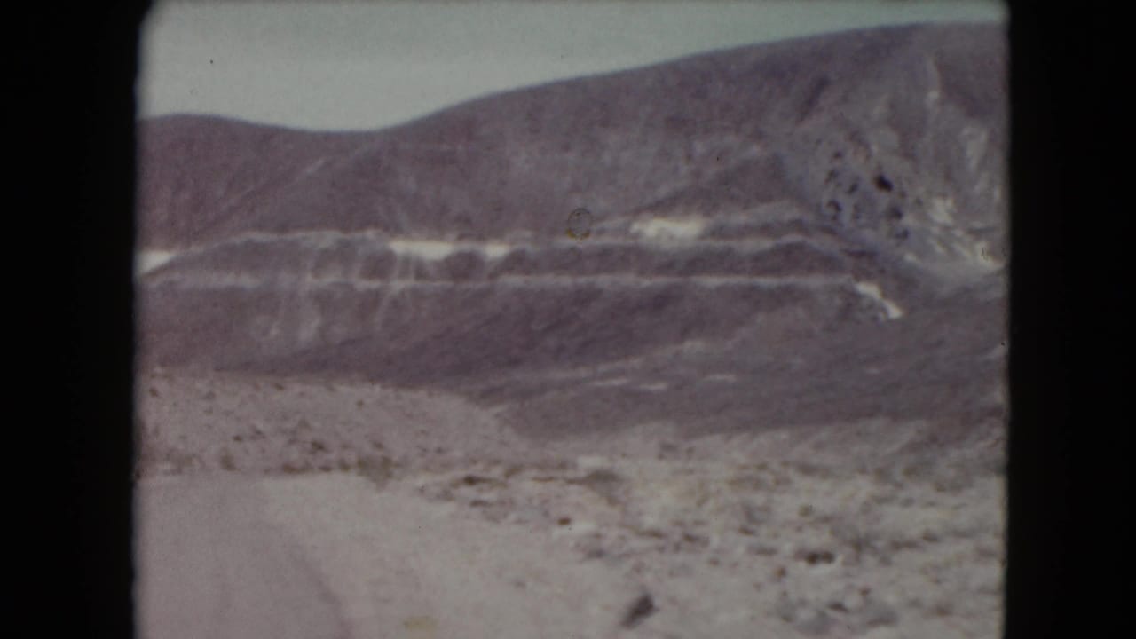 1961 Nevada home-movie view of arid roadside terrain and horizontally banded desert mountains.
