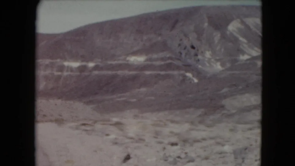 1961 Nevada 8mm frame centered on layered hills, mineral-colored streaks, and sparse rocky desert ground.