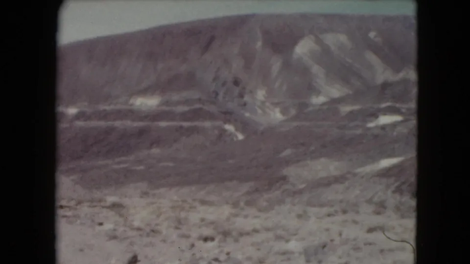1961 Nevada home-movie frame showing a broad mountain slope with light bands above sparse desert terrain.