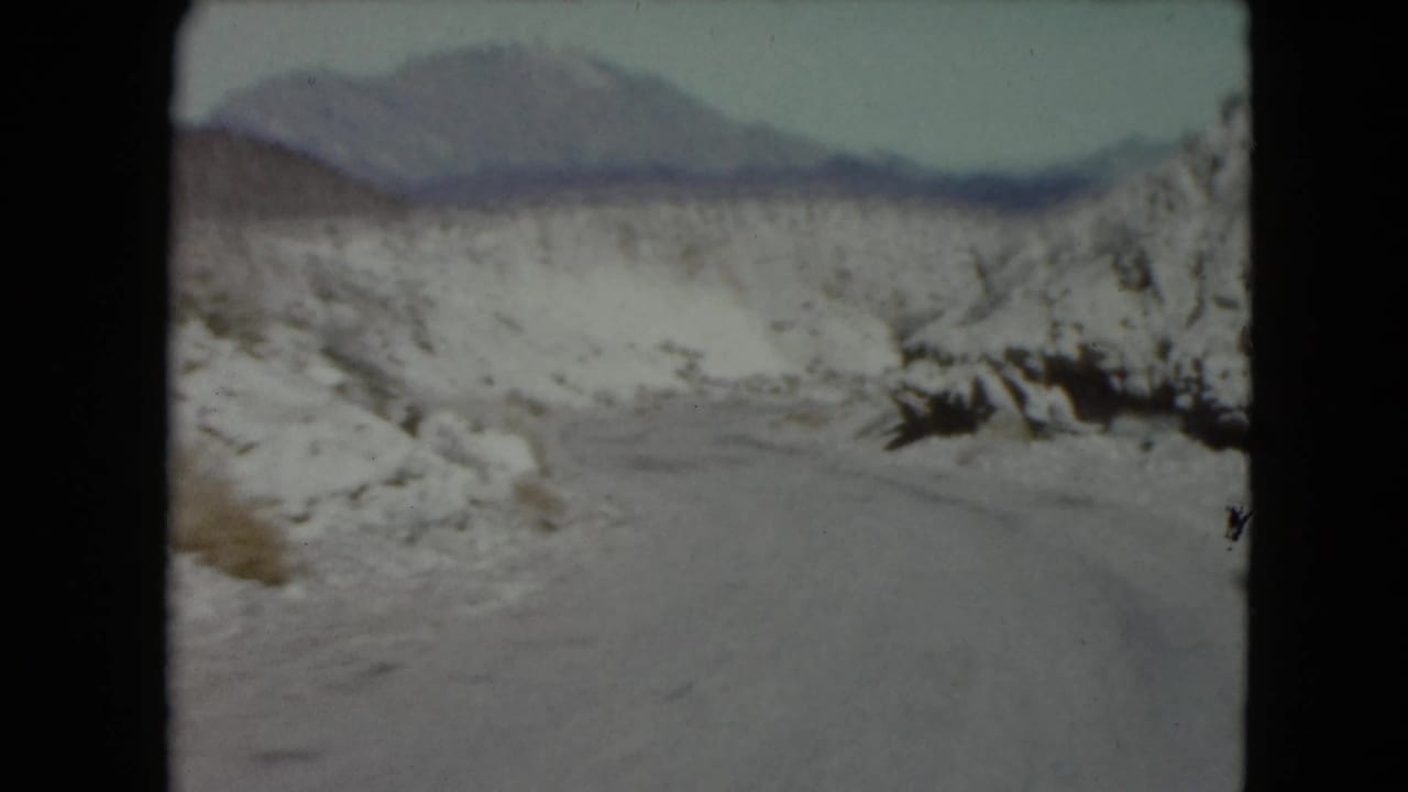 Winding road through snow-dusted hills with distant mountains.