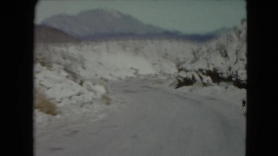 1961 Nevada 8mm frame showing a paved mountain road curving through snow-dusted arid hills toward distant peaks.