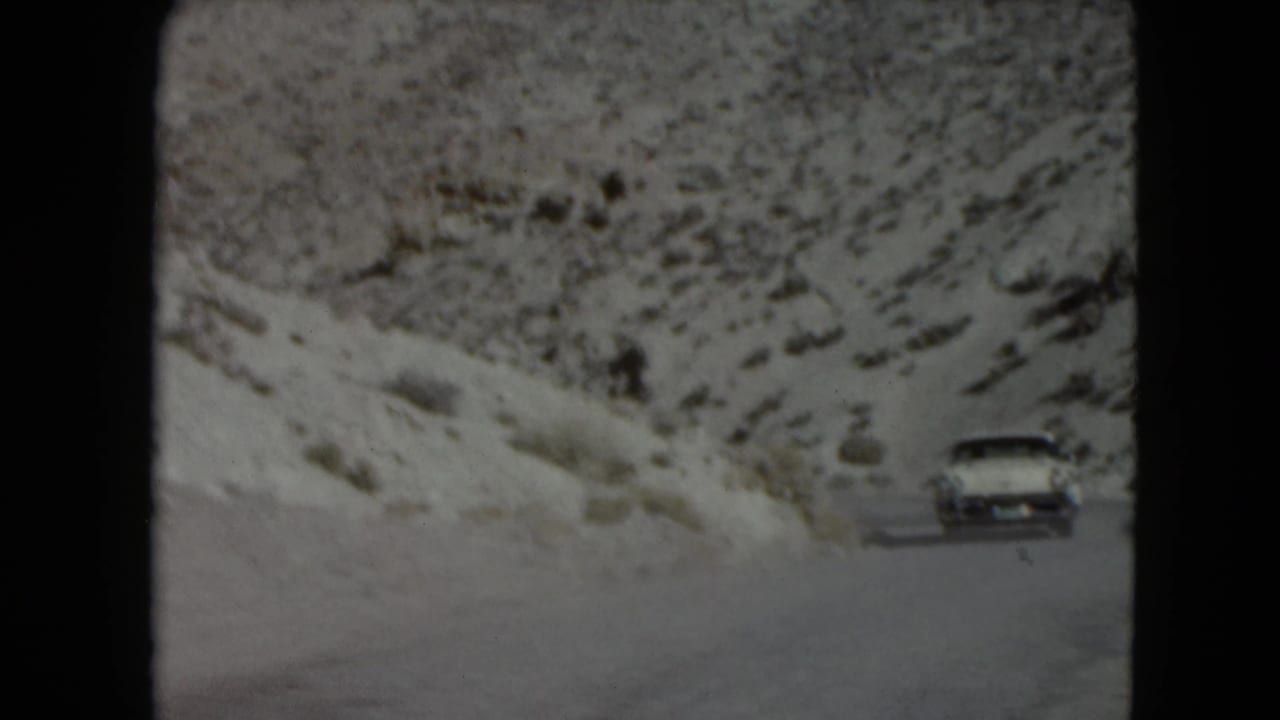 White sedan appears on a snowy mountain road beside rocky slopes.