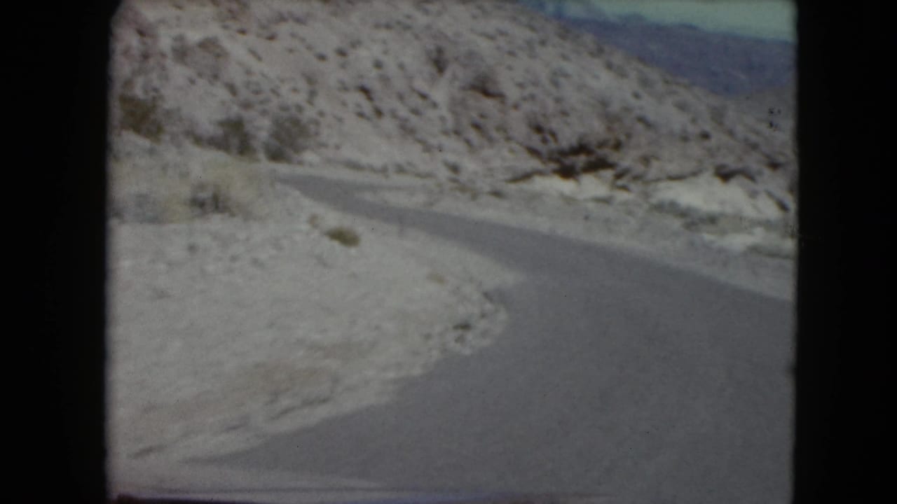 1961 8mm frame of a snowy mountain road, likely in Nevada, bending through rocky winter terrain under a pale sky.