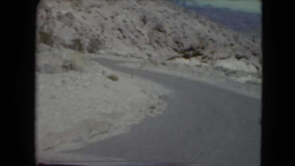 1961 8mm frame of a snowy mountain road, likely in Nevada, bending through rocky winter terrain under a pale sky.