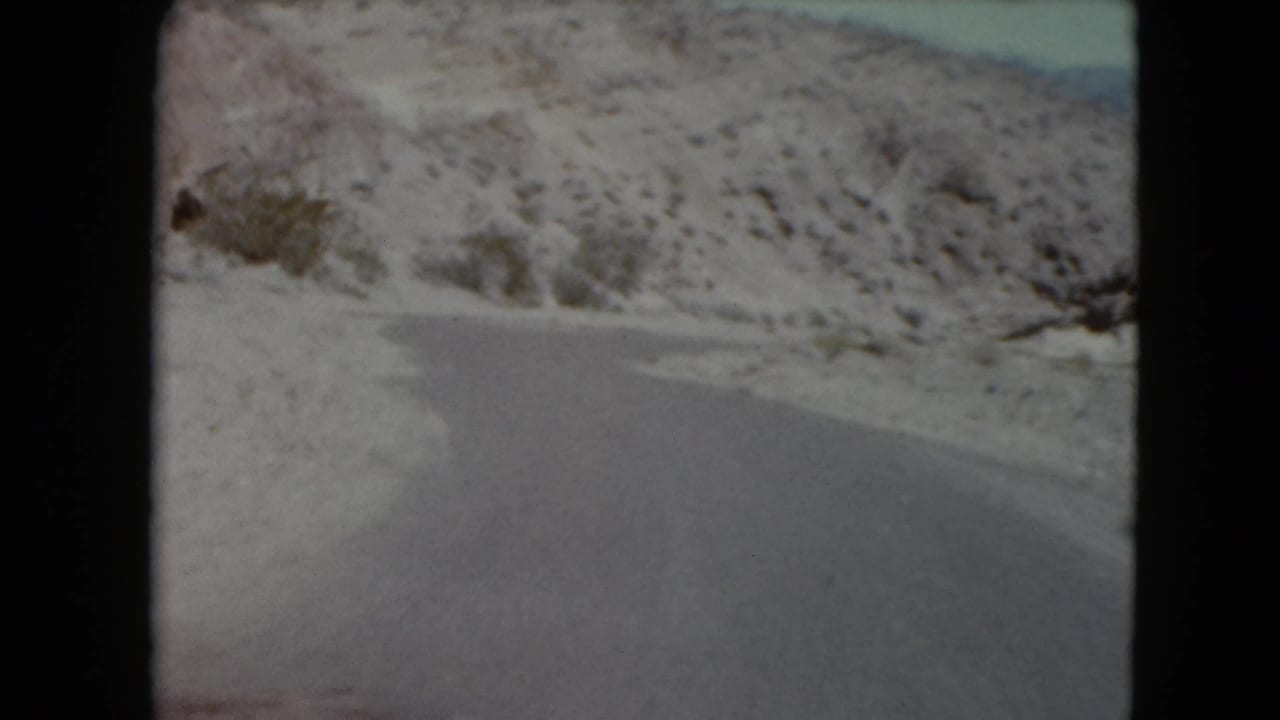 Snow and ice cover the roadside as the 8mm camera looks ahead along a winding mountain road, likely Nevada in 1961.