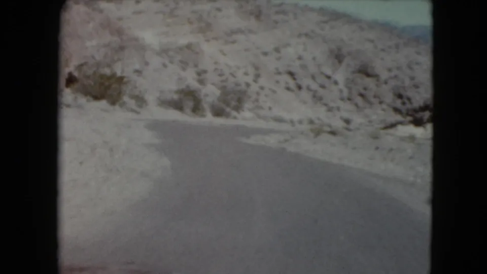 Snow and ice cover the roadside as the 8mm camera looks ahead along a winding mountain road, likely Nevada in 1961.