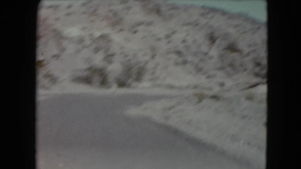 A soft, motion-blurred 8mm view shows snowy roadside terrain and pavement during a winter mountain drive.