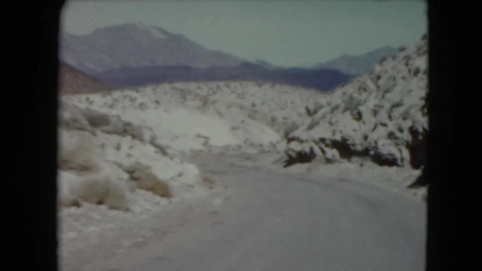 A likely Nevada 1961 8mm frame shows a snow-lined road leading toward distant mountains and open winter terrain.