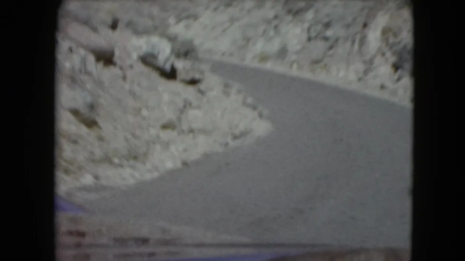 1961 Nevada home-movie frame of a paved road bending through pale rocky desert slopes.