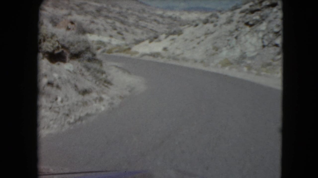 A forward view of a Nevada desert road curving past rocky terrain in 1961 8mm footage.