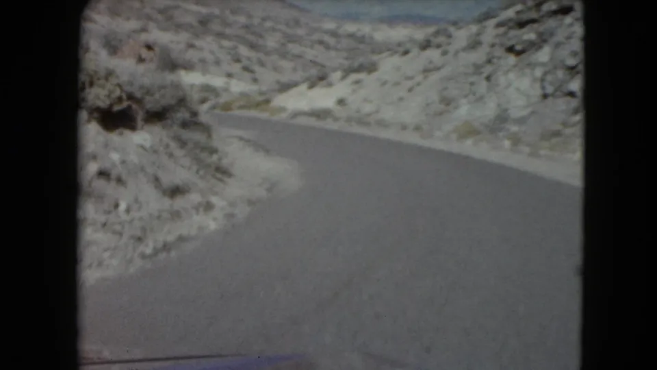 A forward view of a Nevada desert road curving past rocky terrain in 1961 8mm footage.