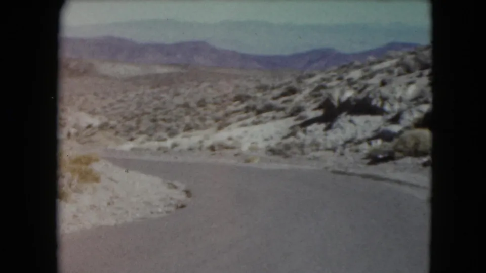 Nevada desert road scene with scrubland and distant mountains in a 1961 travel home movie.