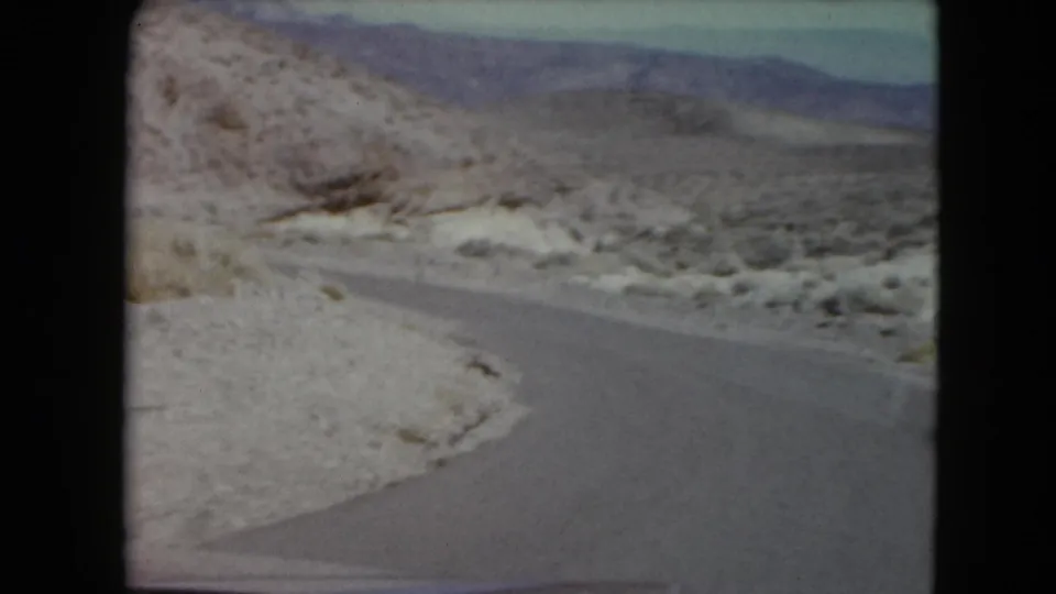 End frame of a 1961 Nevada 8mm road shot, with asphalt curving through scrubby desert toward mountains.