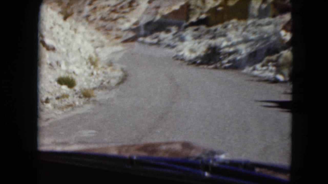 1961 Nevada 8mm home-movie view from inside a vehicle approaching a tight curve between rocky desert slopes.