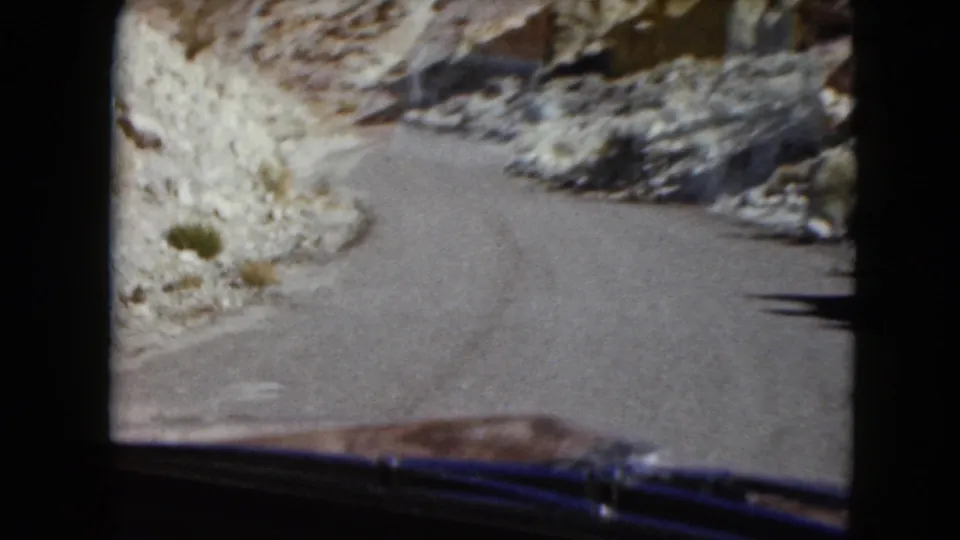 1961 Nevada 8mm home-movie view from inside a vehicle approaching a tight curve between rocky desert slopes.