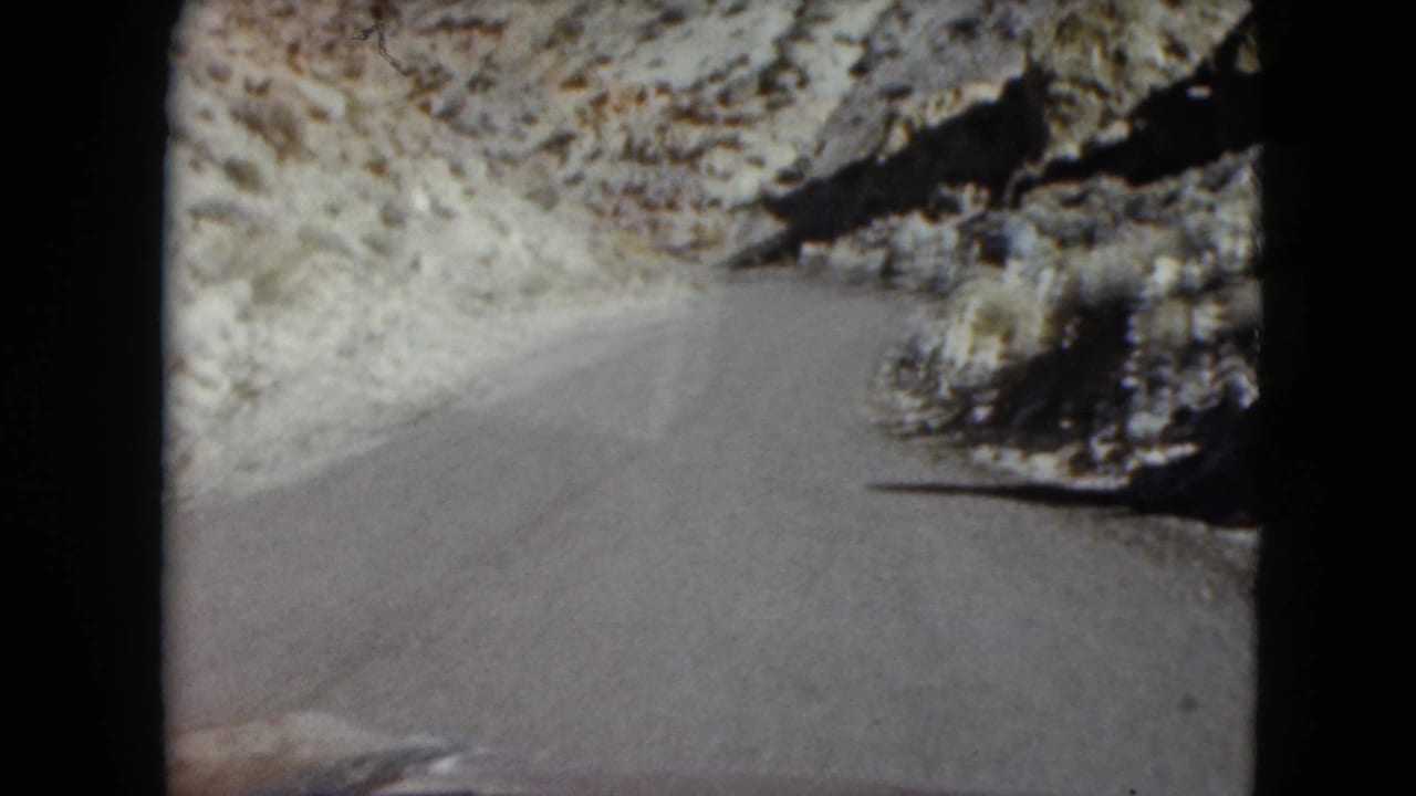 Windshield-facing 1961 Nevada road view as the pavement bends right through dry rocky terrain.