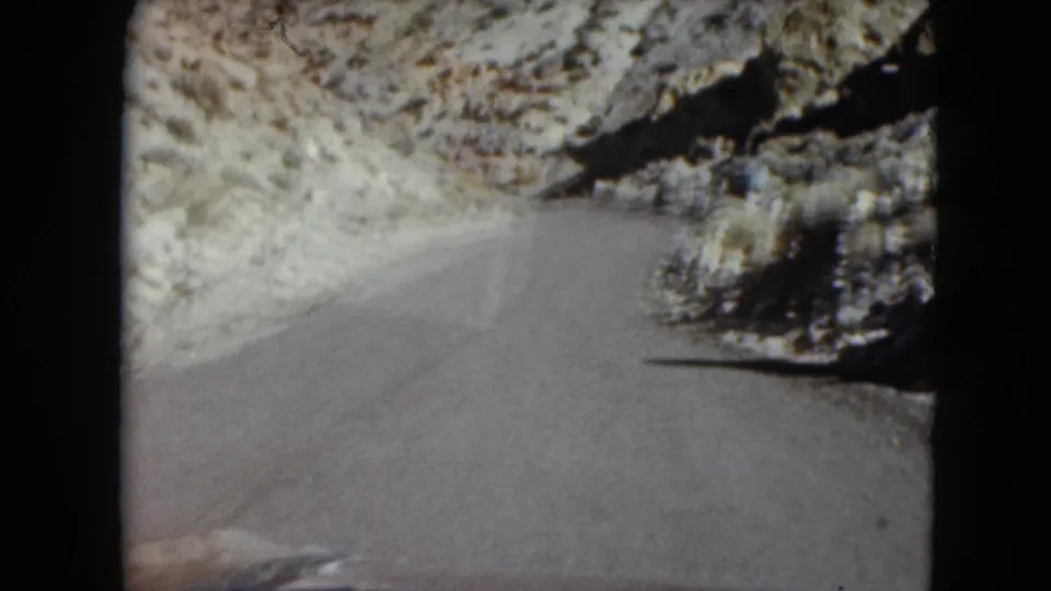 Windshield-facing 1961 Nevada road view as the pavement bends right through dry rocky terrain.