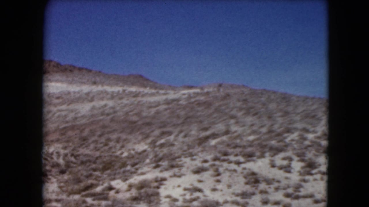 Rolling desert hillside beneath a deep blue sky, framed by dark 8mm film borders.