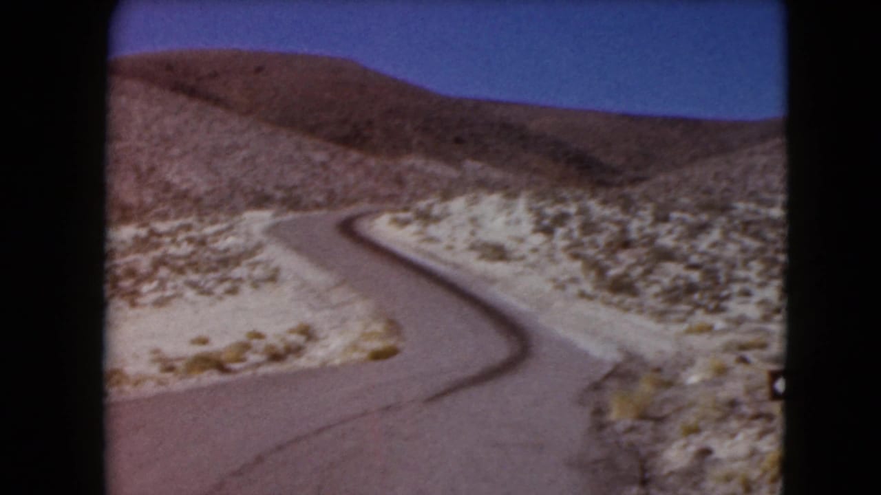 1961 Nevada 8mm frame of a paved road curving through open desert hills beneath a clear blue sky.