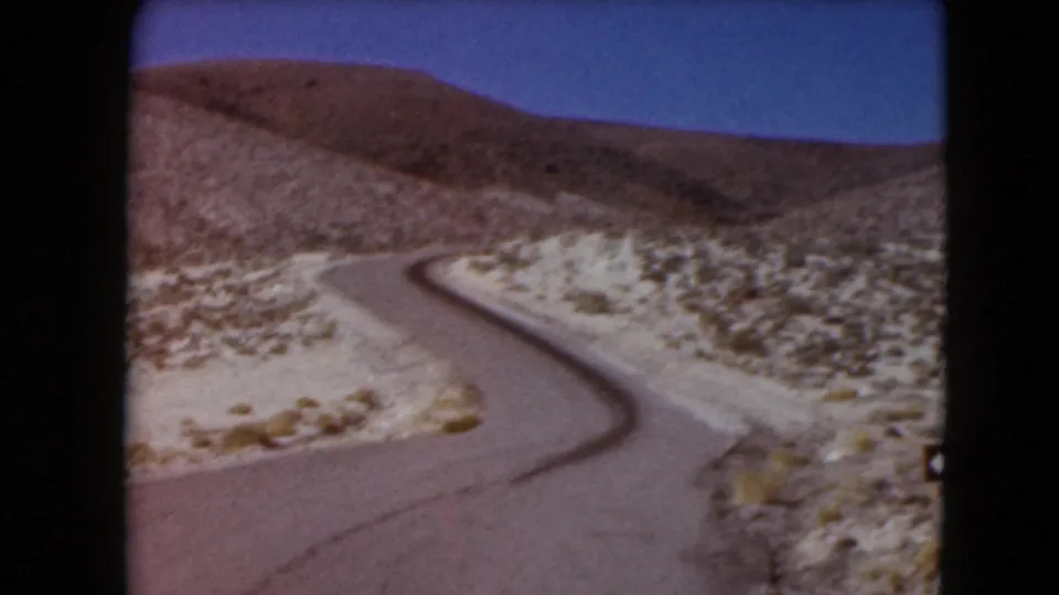1961 Nevada 8mm frame of a paved road curving through open desert hills beneath a clear blue sky.