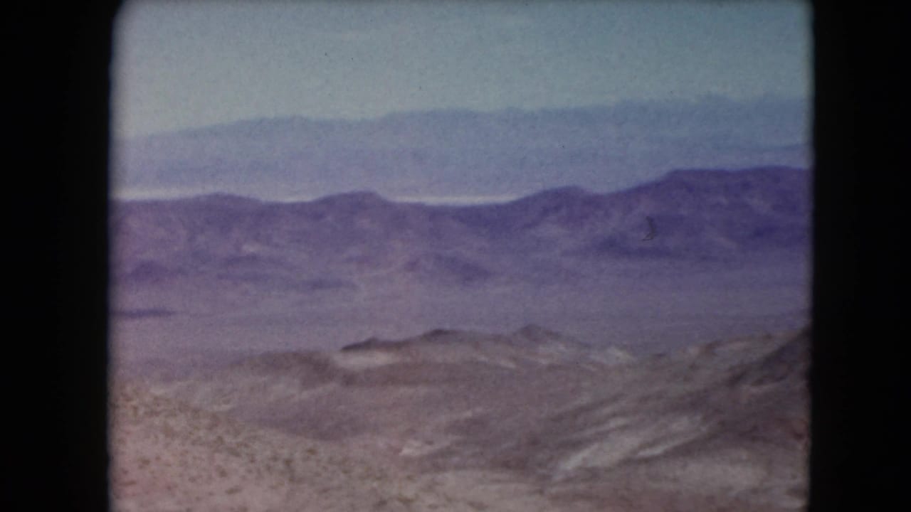 Hazy mountain ranges beyond a rocky Nevada desert slope.