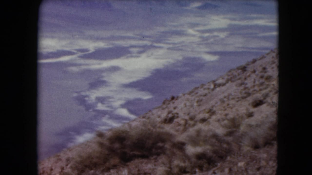 High desert slope overlooking a pale arid valley and distant mountains.