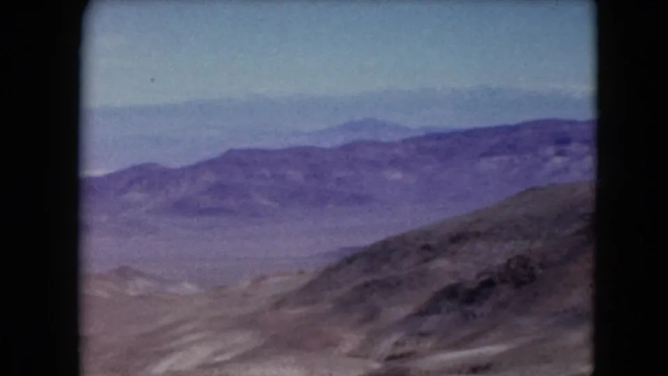 1961 Nevada 8mm frame showing layered purple-toned desert ridges descending into a hazy arid valley.
