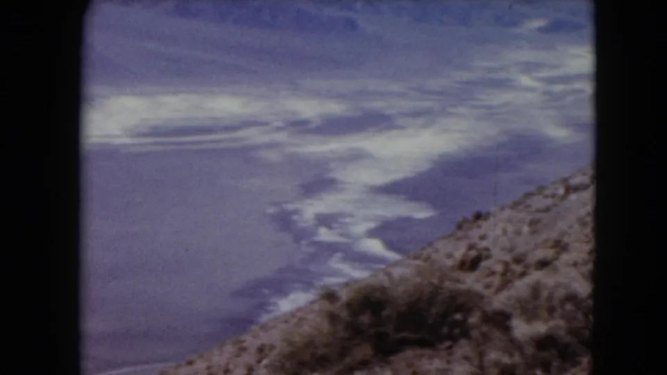 1961 Nevada 8mm aerial view of pale desert water or mineral patterns with a rocky hillside in the foreground.