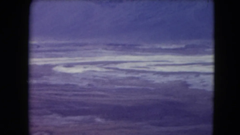 1961 8mm frame with layered clouds over a broad water view, rendered in faded purple-blue color.